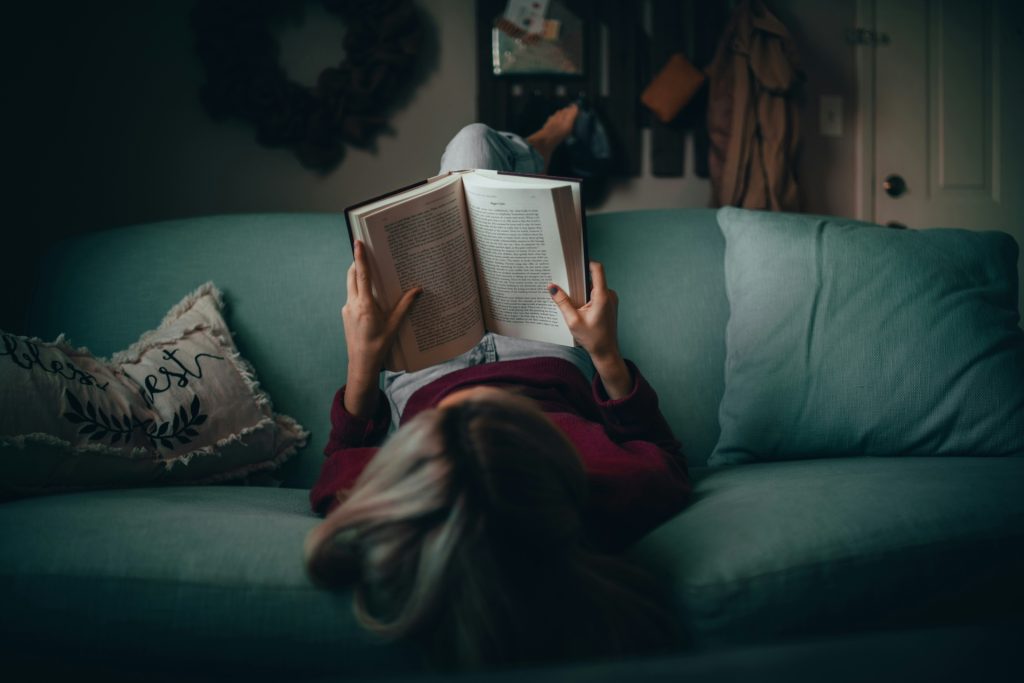 Girl lying on a couch reading a book upside down, reflecting creativity, imagination, and alternative ways of focusing, related to ADHD.